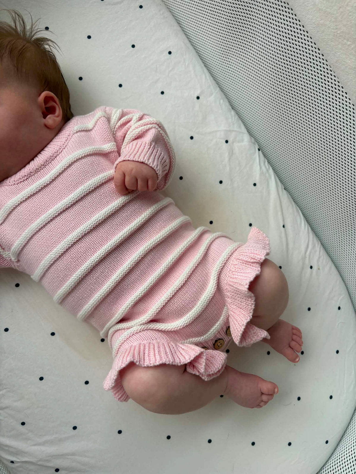 A baby wearing a pink ribbed knit romper with white stripes and ruffled trim.