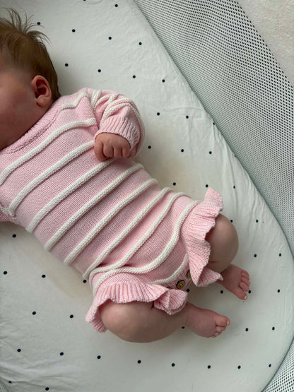 A baby wearing a pink ribbed knit romper with white stripes and ruffled trim.