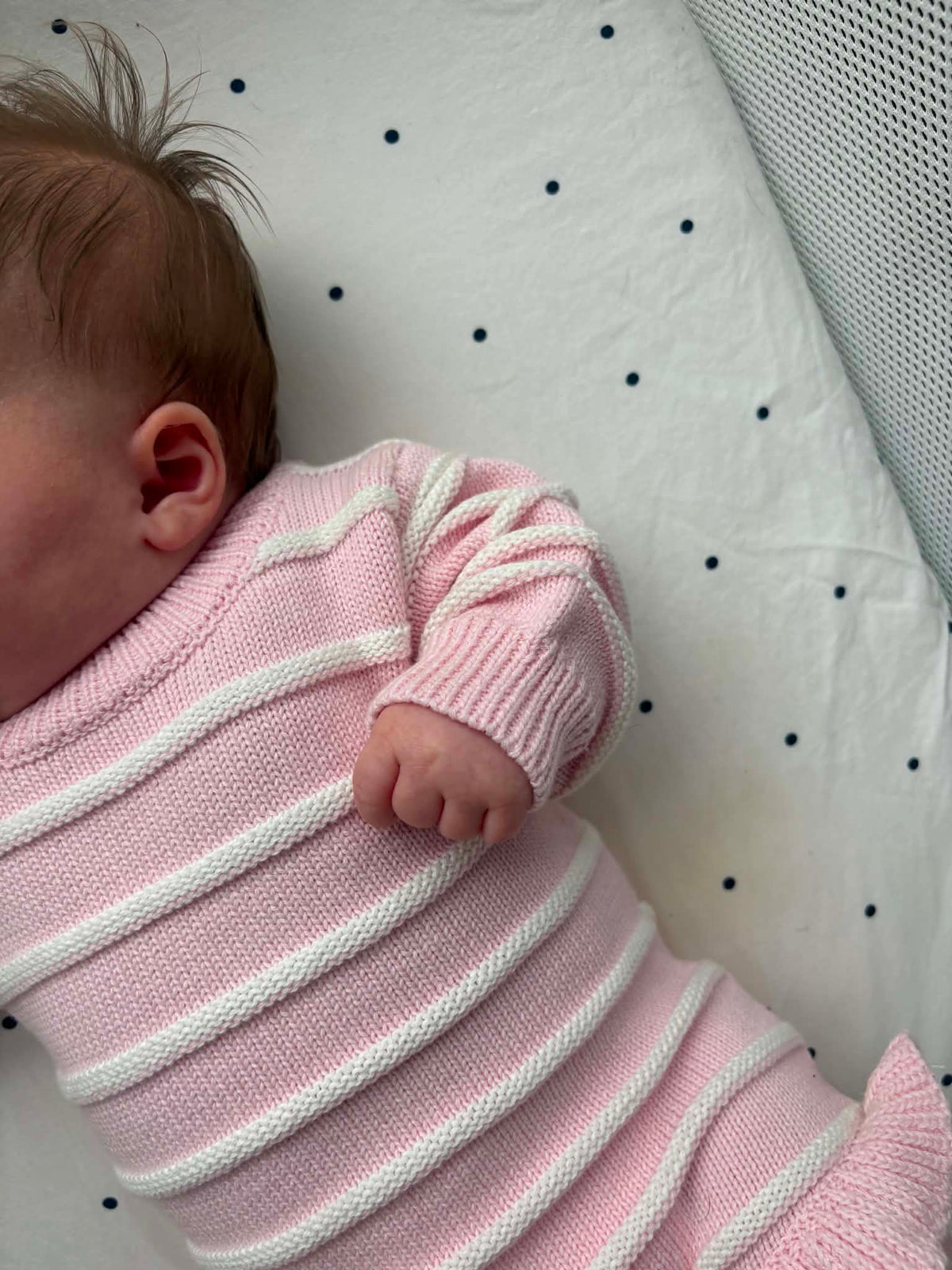 A close-up of a baby wearing a pink and white striped knit long-sleeve romper
