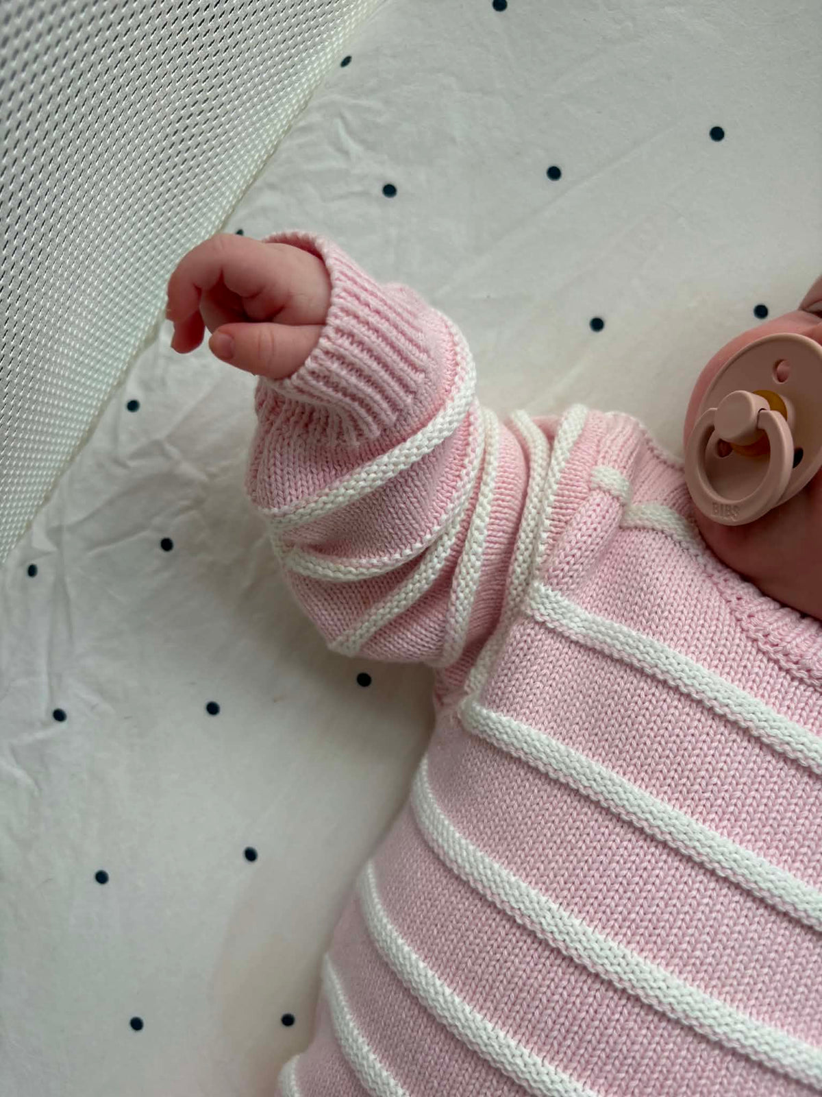 A close-up of a baby wearing a pink and white striped knit romper