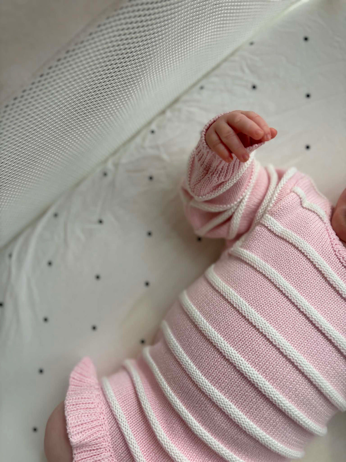 A close-up of a baby wearing a pink ribbed knit bodysuit with white stripes