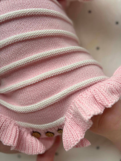 Close-up of a pink knitted newborn romper with white horizontal stripes and a ruffled hem