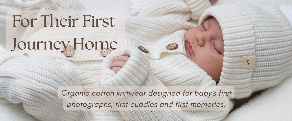 A sleeping newborn baby wrapped in cream-colored organic cotton knitwear, including a knitted hat and matching outfit, with overlaid text reading 'For Their First Journey Home' and 'Organic cotton knitwear designed for baby's first photographs, first cuddles and first memories.'.