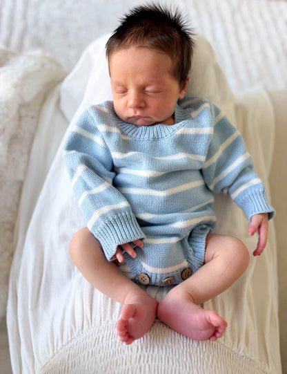 A sleeping newborn baby wearing a light blue and white striped knit romper, lying on a white textured blanket.