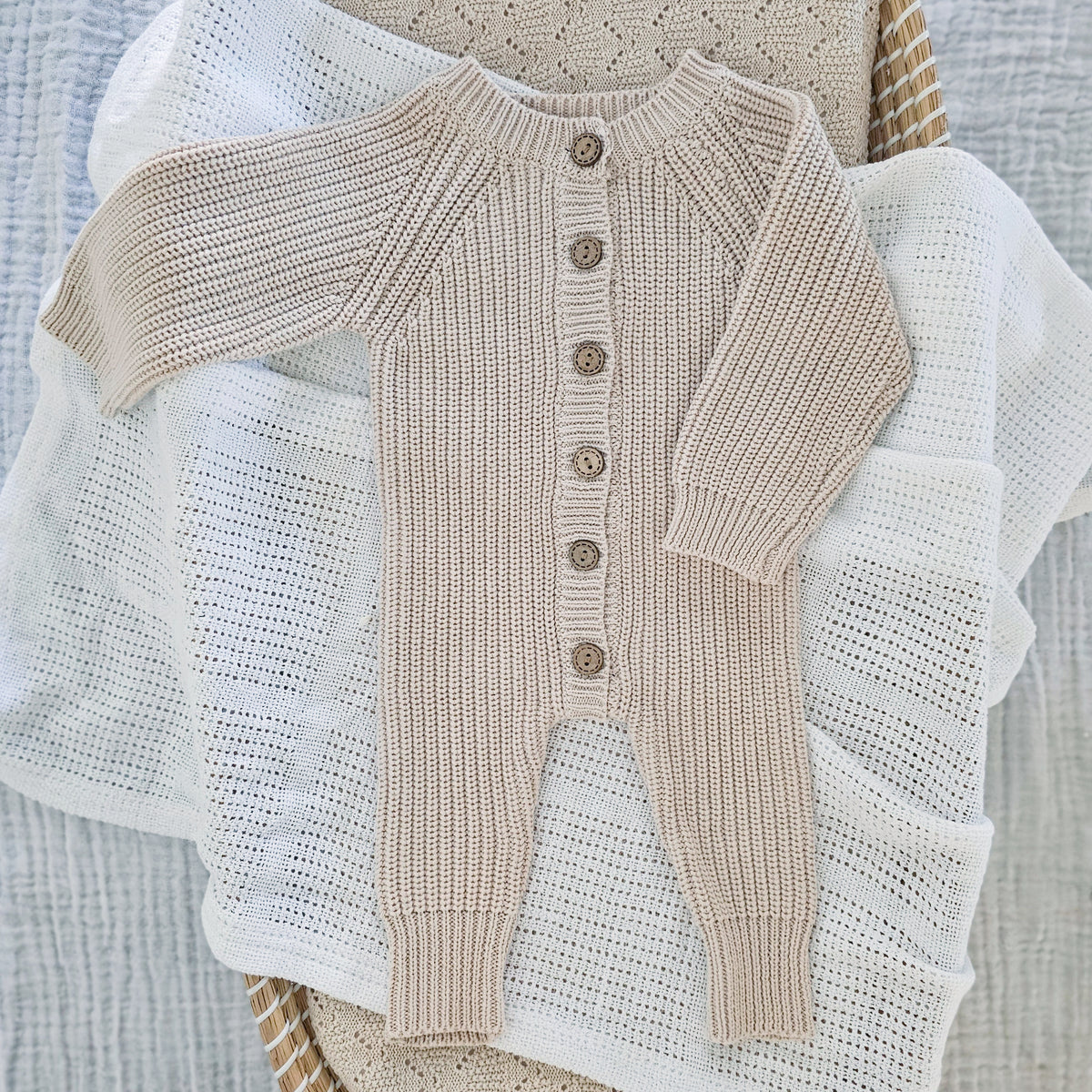 A taupe-colored chunky knit body suit for babies, with wooden buttons, 